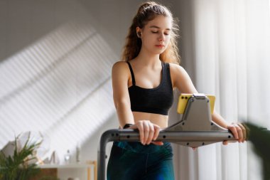 Ev antrenmanı. Koşu bandında koşan genç bir kadın..