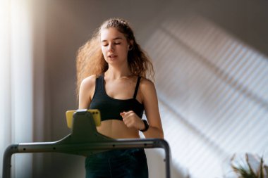 Ev antrenmanı. Koşu bandında koşan genç bir kadın..