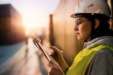 Beyaz şapkalı kadın endüstriyel mühendis konteyner terminalinde çalışıyor..