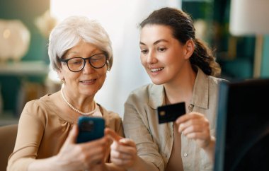 Genç ve yaşlı kadınlar online alışveriş için bilgisayar kullanıyorlar. Kızı evde annesine yardım ediyor..