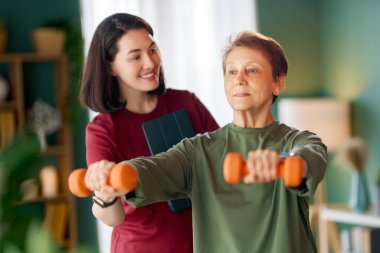 Kıdemli kadın halter egzersizi yapıyor. Evde fizik tedaviye yardım eden bir hemşire.