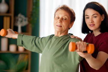 Kıdemli kadın halter egzersizi yapıyor. Evde fizik tedaviye yardım eden bir hemşire.