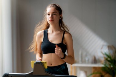 Ev antrenmanı. Koşu bandında koşan genç bir kadın..