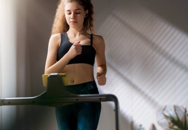 Ev antrenmanı. Koşu bandında koşan genç bir kadın..