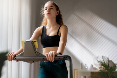 Ev antrenmanı. Koşu bandında koşan genç bir kadın..