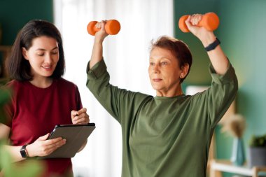 Kıdemli kadın halter egzersizi yapıyor. Evde fizik tedaviye yardım eden bir hemşire.