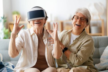 Evde VR gözlük takan iki yaşlı kadın konsol oyunu oynuyor..