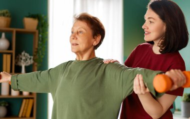 Kıdemli kadın halter egzersizi yapıyor. Evde fizik tedaviye yardım eden bir hemşire.