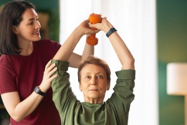 Kıdemli kadın halter egzersizi yapıyor. Evde fizik tedaviye yardım eden bir hemşire.