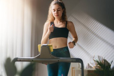 Ev antrenmanı. Koşu bandında koşan genç bir kadın..