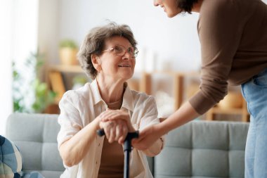 Mutlu hasta ve bakıcı birlikte vakit geçiriyor. Yaşlı kadın baston tutuyor..