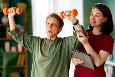 Kıdemli kadın halter egzersizi yapıyor. Evde fizik tedaviye yardım eden bir hemşire.