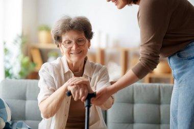 Mutlu hasta ve bakıcı birlikte vakit geçiriyor. Yaşlı kadın baston tutuyor..