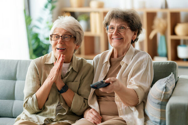 Senior women watching TV, movies. Retirees spending time at home.