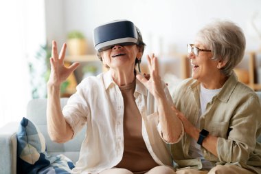 Evde VR gözlük takan iki yaşlı kadın konsol oyunu oynuyor..