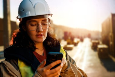 Beyaz şapkalı kadın endüstriyel mühendis konteyner terminalinde çalışıyor..