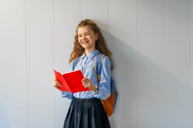 Gri duvar arkasında duran sevimli, mutlu bir genç. Sırt çantalı çocuk, kız okula dönmeye hazır.. 