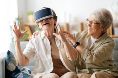 Evde VR gözlük takan iki yaşlı kadın konsol oyunu oynuyor..