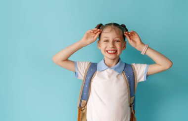 Açık mavi arka planda duran sevimli mutlu genç. Sırt çantalı çocuk, kız okula dönmeye hazır..