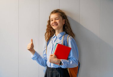 Gri duvar arkasında duran sevimli, mutlu bir genç. Sırt çantalı çocuk, kız okula dönmeye hazır.. 