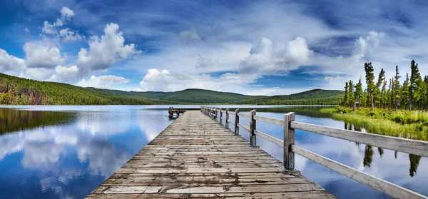 美丽的山湖 有倒影和木制码头 淡淡的白云和蔚蓝的天空映照在静谧的水中 — 图库照片