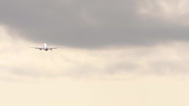 Rear view of a passenger jet plane climbing after takeoff. Airplane silhouette at sunset or sunrise
