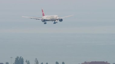 SOCHI, RUSSIA - AUGUST 03, 2022: Boeing 777 of Nordwind Airlines descending before landing at Sochi airport. Airplane on the background of the city. Tourism and travel concept