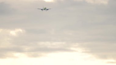 Long shot of airplane approaching before landing at cloudy sky. Tourism and aviation concept
