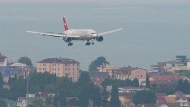 SOCHI, RUSSIA - AUGUST 03, 2022: Boeing 777 of Nordwind Airlines descending before landing at Sochi airport. Airplane on the background of the city. Tourism and travel concept