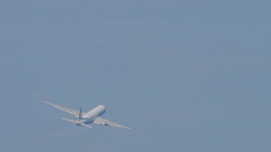 Unrecognizable widebody aircraft climb after takeoff, fly away, long shot. Airliner in the blue sky. Airplane flying, bottom view