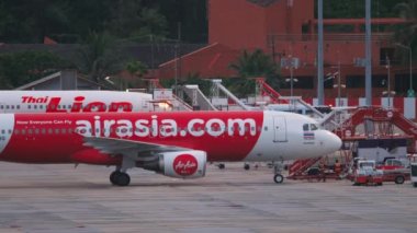 PHUKET, THAILAND - NOVEMBER 28, 2019: Side view of a tractor towing an plane AirAsia on the airfield of Phuket airport. Tourism and travel concept