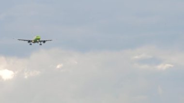 Unrecognizable aircraft with Green livery in the sky. Airplane approaching for landing, front view. Slow motion, airliner is flying