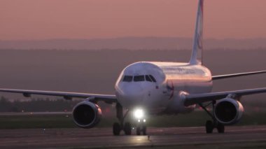 KAZAN, RUSSIA - AUGUST 05, 2022: Cinematic footage of a Ural Airlines passenger plane taxiing on the runway, sunset or dawn. Airplane on the taxiway at sunrise