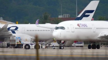 PHUKET, THAILAND - NOVEMBER 26, 2017: Tractor towing Airbus A350 of Thai Airways on the runway at Phuket airport, medium shot. Tourism and travel concept