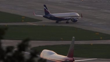 SOCHI, RUSSIA - JULY 28, 2022: Airbus A320 of Aeroflot taxiing to the runway Sochi airport, sunset or dawn. Boeing 747 of Rossiya on the taxiway, foreground. Tourism and travel concept