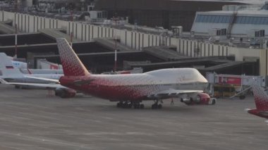 SOCHI, RUSSIA - JULY 28, 2022: Tractor pulling Boeing 747 of Rossiya on the runway at Sochi airport at sunset. Jumbo jet on the airfield. Tourism and travel concept