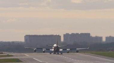 Cinematic footage of a heavy wide-body aircraft decelerating after landing, rear view. Flaps up when decelerating. Sunset or dawn on the airfield. Tourism and travel concept
