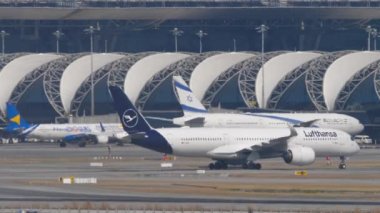 BANGKOK, THAILAND - JANUARY 19, 2023: Passenger plane Airbus A350 of Lufthansa taxiing at Suvarnabhumi airport. Haze on a hot day on the airfield. Row of planes docked at the terminal. Travel concept