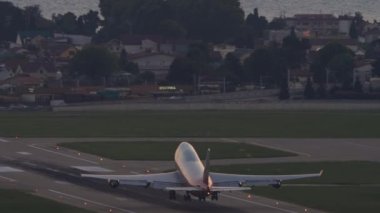 Huge four-engine passenger plane takeoff, sunset pink sky. Jumbo jet departure, rear view. Passenger flight. Flight over the sea