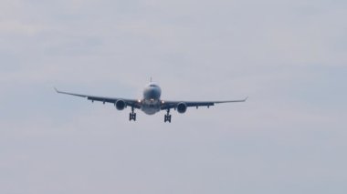 Bottom view, silhouette of a passenger jet aircraft approaching for landing against a cloudy gray sky. Tourism and aviation concept