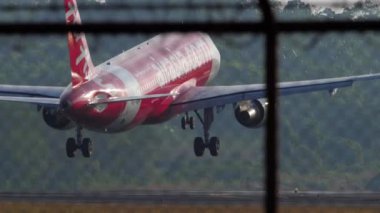 PHUKET, THAILAND - JANUARY 27, 2023: Jet passenger plane Airbus A320 of AirAsia landing, touching the runway and braking. Flight arrival. View of the airfield through the airport fence