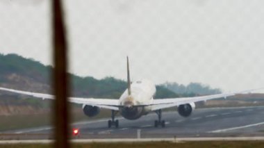 Footage of an airplane speeding up and taking off, rear view. Passenger plane flies away, view through the fence