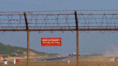 Red sign Restricted area. Long shot of jet airplane take off, departure at Phuket airport. Charter passenger flight. Travel concept