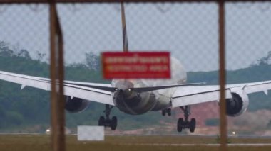 PHUKET, THAILAND - JANUARY 28, 2023: Passenger aircraft Etihad 787 Dreamliner braking after landing at Phuket airport, rear view. Runway touchdown. Flaps up, speed down. Airfield through the fence