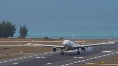 PHUKET, THAILAND - 7 Şubat 2023: Airbus A330, Cathay Pacific B-LAK Phuket Havaalanına indikten sonra fren yapıyor. Uçak pistte, ön manzara. Uçak ve denizin görüntüsü. Beneklenme