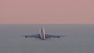 Huge four-engine passenger plane takeoff, sunset pink sky. Jumbo jet departure, rear view. Passenger flight. Flight over the sea