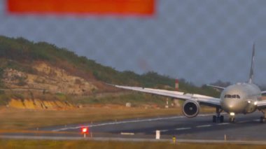 PHUKET, THAILAND - JANUARY 22, 2023: Plane of ETIHAD braking after landing at Phuket airport. View through the fence. Airplane on the airfield. Flaps up, speed down. Travel concept
