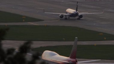 SOCHI, RUSSIA - JULY 28, 2022: Airbus A320 of Aeroflot taxiing to the terminal at Sochi airport, sunset or dawn. Boeing 747 of Rossiya on the taxiway, foreground. Tourism and travel concept