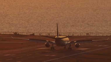 Uçak silueti gün batımında denizin arka planında fren yapıyor. Arka planda bir jet uçağının sinematik çekimi. Turizm ve seyahat kavramı