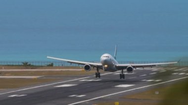 PHUKET, THAILAND - FEBRUARY 07, 2023: Cathay Pacific 'in ticari uçak Airbus A330' u Phuket Havalimanı 'na iniş ve frenleme. Uçak pistte, ön manzara. Havaalanı, deniz arka planı
